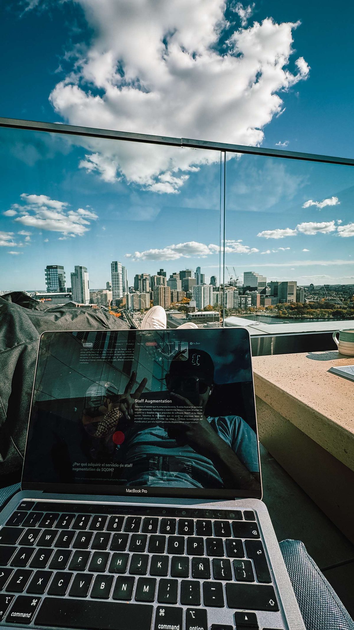 A laptop on a rooftop ledge above the Boston skyline, with a staff augmentation page on screen